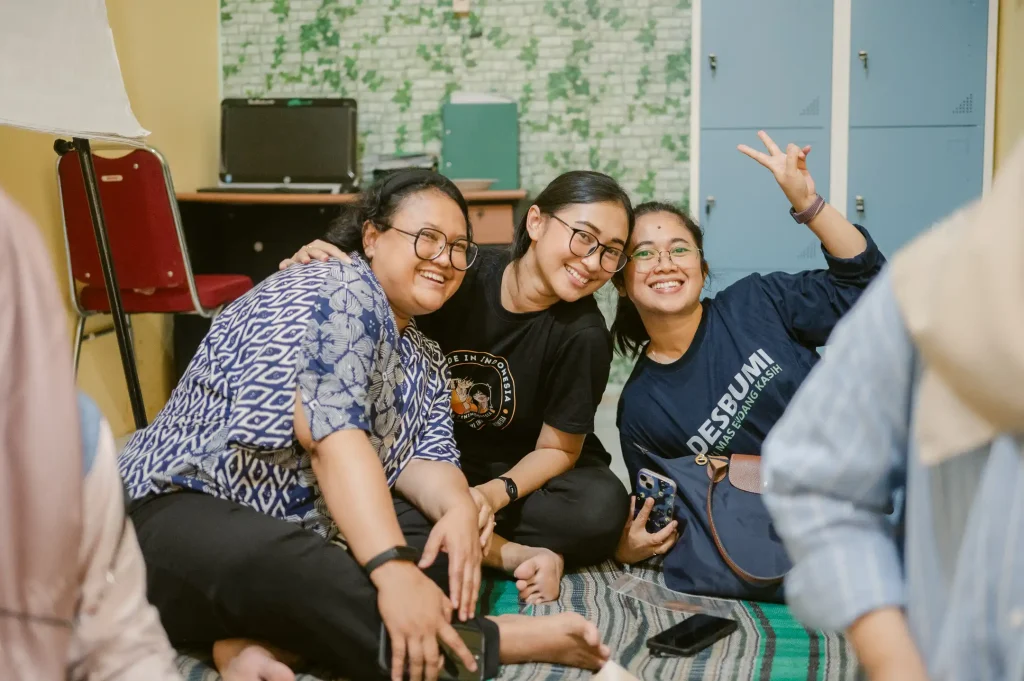 Three Indonesian SCILLS program beneficiaries wave to the camera while smiling.